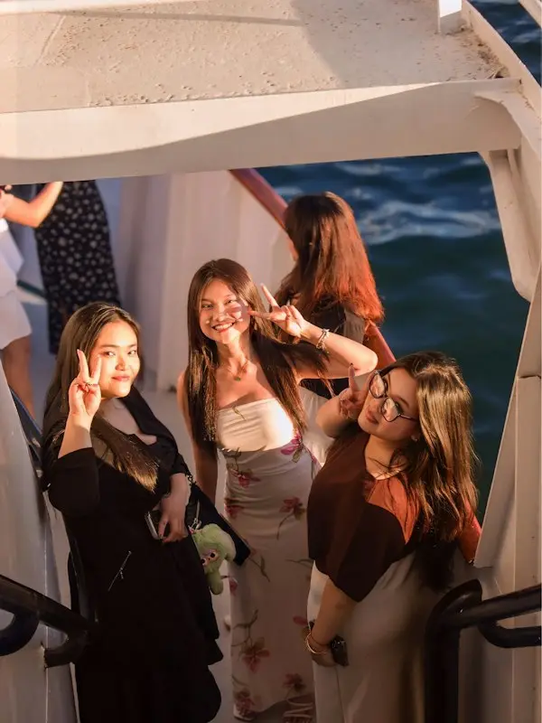 Three friends making peace signs on a boat at golden hour