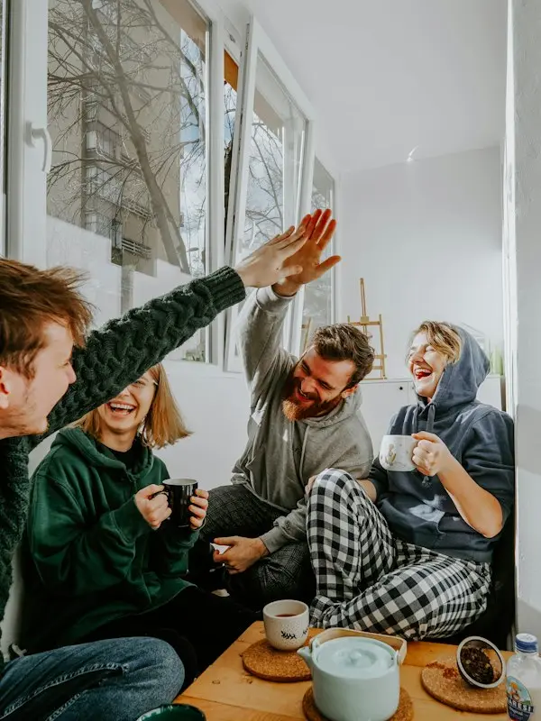 Four friends laughing and high-fiving over coffee
